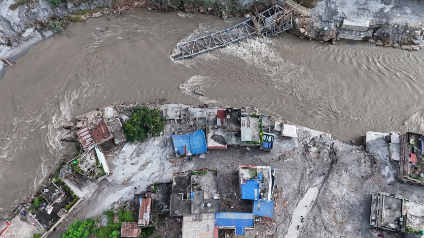 An aerial view shows A collapsed bridge and damaged settlements debris and mud covering an area following flash floods on August 28, in DeviGhat village, Nepal.