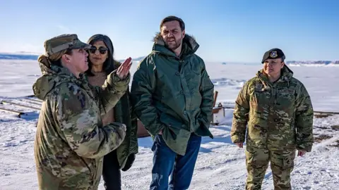 Getty Images JD Vance and his wife Usha Vance pictured with the commander of the US military's Pituffik Space Base in Greenland in March. They are surrounded by a snowy landscape.