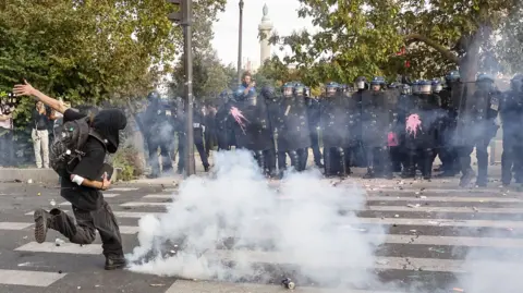 EPA A protester kicks a tear gas canister as police watch on during disturbances in Paris on 6 October